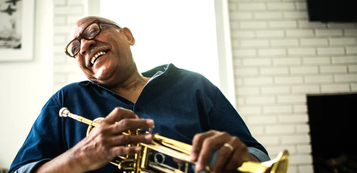 Screened-back image of an older man laughing and holding a trumpet